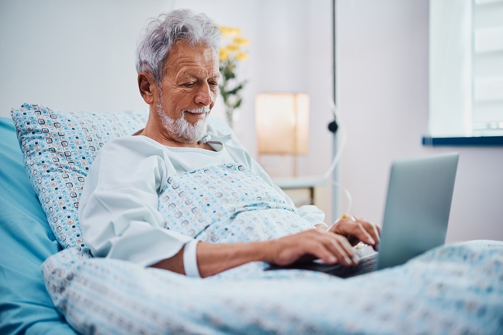 Smiling hospitalized senior man surfing the net on laptop.