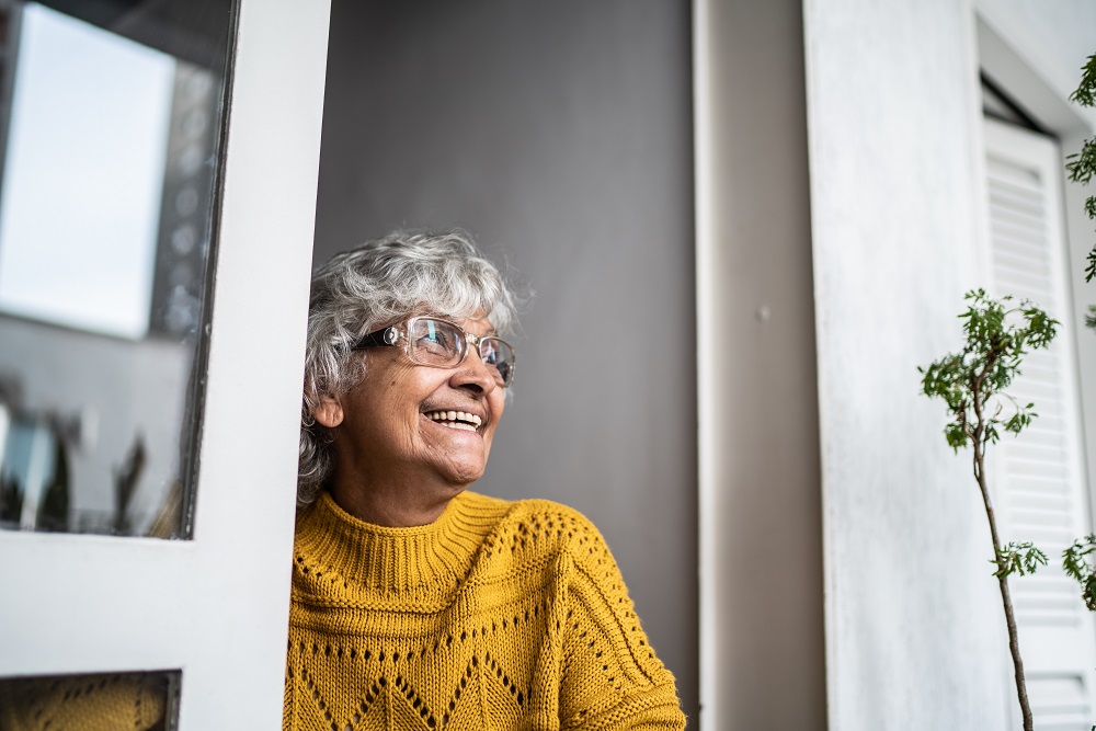 Contemplative senior woman looking through window at home